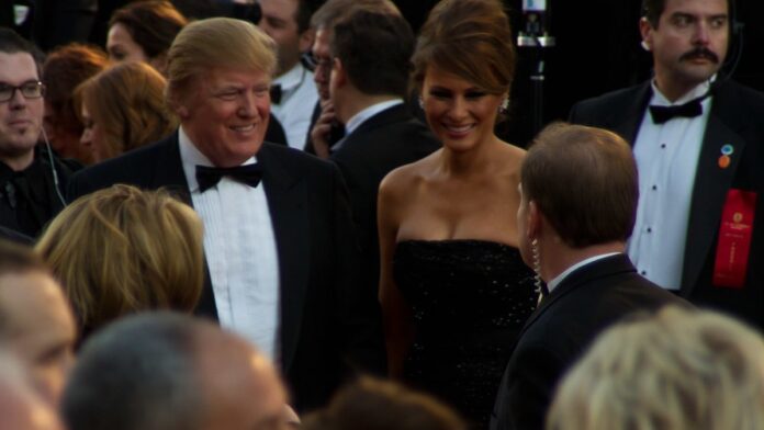 Donald Trump gesticula durante discurso em um pódio, com bandeiras dos EUA ao fundo.
