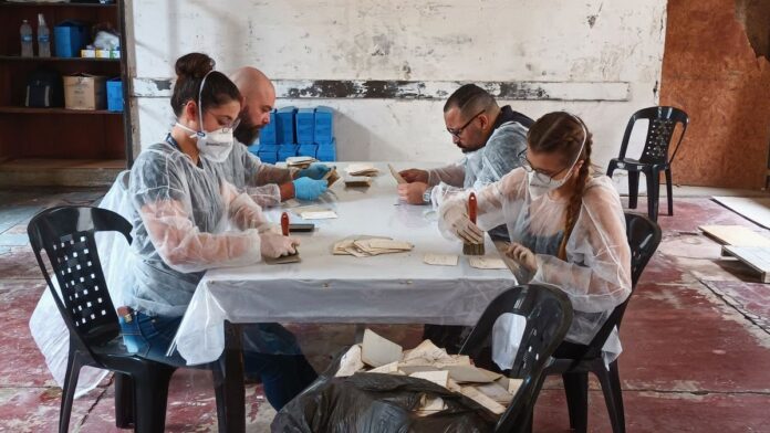 Caixas de arquivos empilhadas em uma estante metálica antiga, com documentos históricos em papel envelhecido.