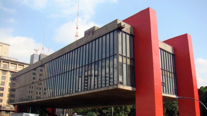 Fachada de uma escola com crianças ao fundo em um pátio, simbolizando o ambiente educacional.