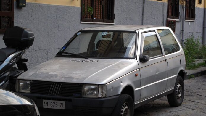 Fiat Uno Mille clássico, de cor sólida, estacionado em uma rua urbana, visto de frente em ângulo levemente lateral.