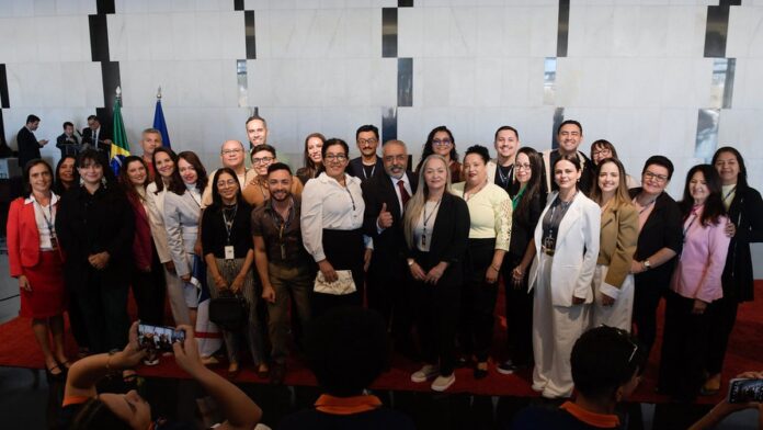 Foto em close de uma policial militar fardada, sorrindo, em um registro profissional de ambiente interno.