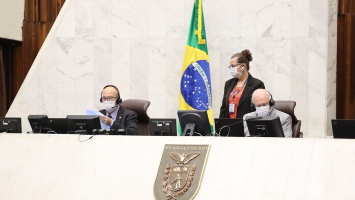 Pessoas sentadas em mesas de reunião participam de palestra sobre crédito, com projetor e logos institucionais ao fundo.