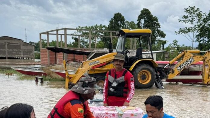 Barcos transportam cestas básicas e equipes de socorro em área alagada pelo Rio Juruá, com casas submersas ao fundo.