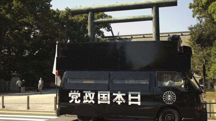 Cerejeiras em flor sob céu azul, com pétalas rosadas cobrindo os galhos de forma densa em um parque japonês.