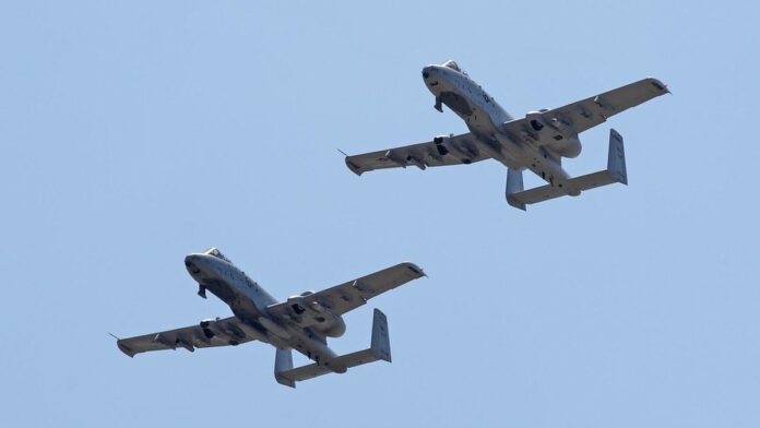 Avião militar em chamas sobrevoando o mar, com uma coluna de fumaça negra subindo ao horizonte no Golfo Pérsico.