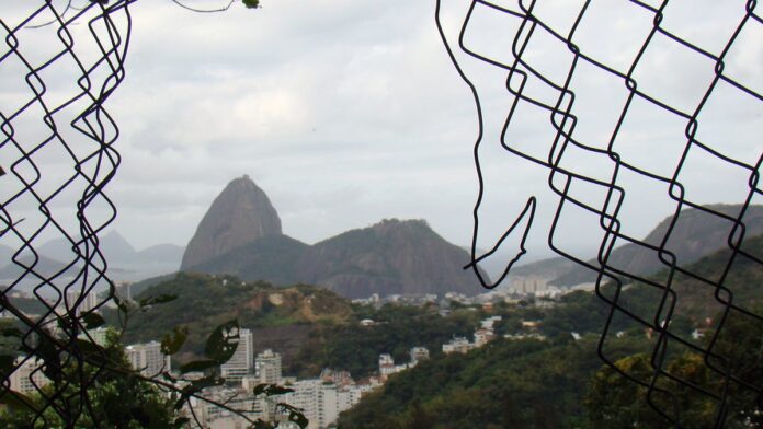 justi-a-pro-be-constru-o-de-tirolesa-no-p-o-de-a-c Vista panorâmica do Pão de Açúcar, no Rio de Janeiro, com seus morros cercados por vegetação e mar ao fundo.