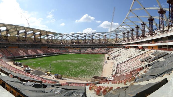 Árbitro de futebol em campo, vestindo uniforme esportivo e segurando uma placa de substituição eletrônica.
