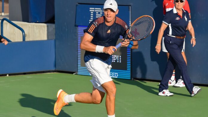 Tenista Marco Trungelliti sorri em quadra, segurando sua raquete após partida, vestindo uniforme esportivo.