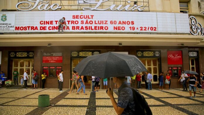Fachada iluminada de um antigo cinema de rua com letreiro neon e cartazes de filmes clássicos em exposição no MIS.