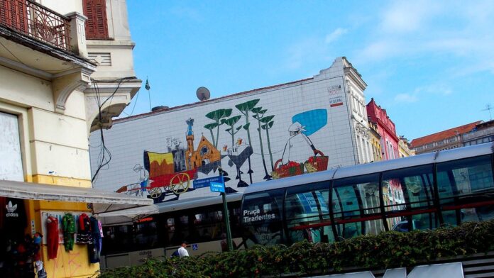 painel-de-poty-lazzarotto-sobre-saneamento-complet Painel em relevo de Poty Lazzarotto, com figuras humanas estilizadas em tons terrosos, instalado em parede de concreto.