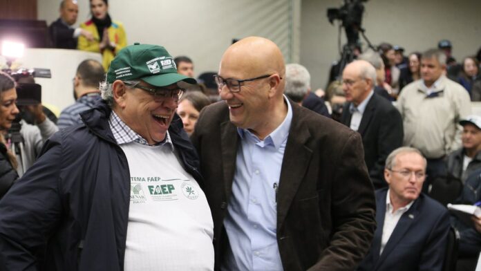 Profissional de saúde aplicando vacina no braço de um idoso em uma unidade de saúde no Paraná.