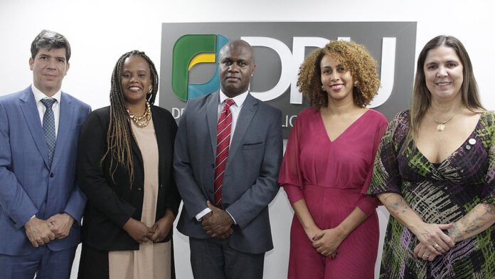 Membros do Partido Novo posam para foto em evento político, em frente a uma bandeira do Brasil e banners da sigla.