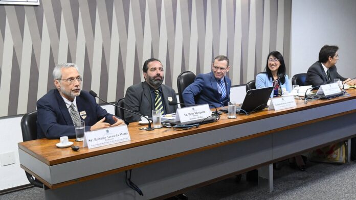 pix-clim-tico-economista-prop-e-aux-lio-para-v-tim Pessoas caminham por uma rua alagada, carregando pertences pessoais após uma enchente em área urbana.
