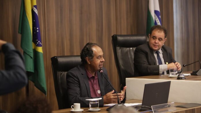 Corredores de diversas idades praticando exercício em uma rua asfaltada ao ar livre durante o dia.