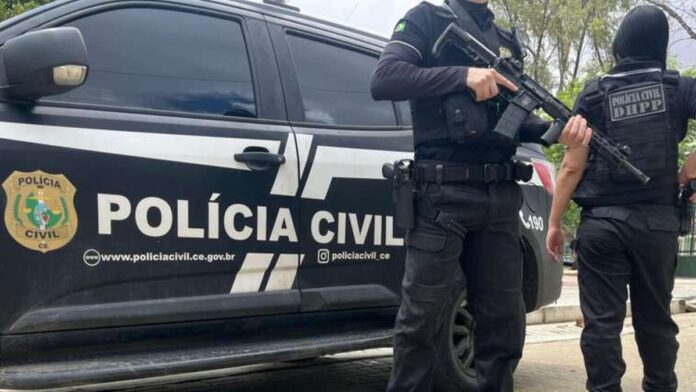 Agentes da Polícia Civil com uniformes táticos posicionados ao lado de dois suspeitos algemados em uma área urbana.