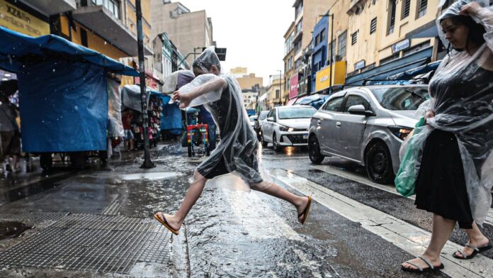 Pessoas segurando guarda-chuvas abertos sob céu nublado e cinzento em uma rua movimentada.
