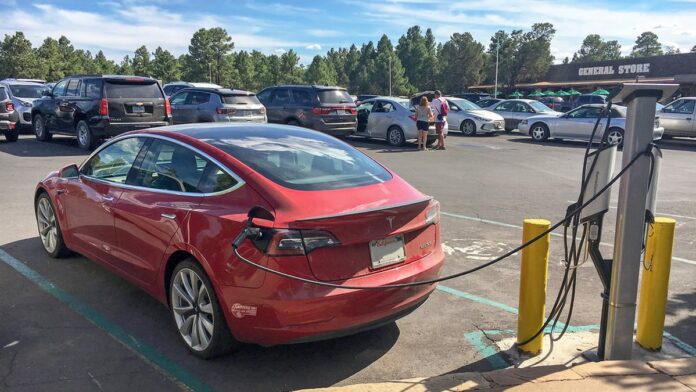 Carro elétrico conectado a uma estação de carregamento moderna em um posto de serviço ao ar livre.