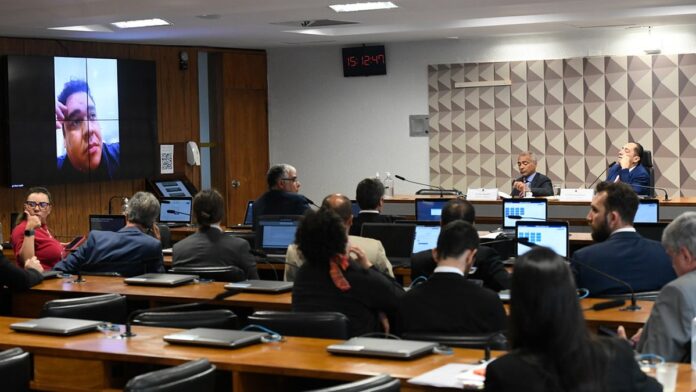 Homem de meia-idade com expressão séria veste terno escuro, posando para foto de identificação policial contra fundo cinza.