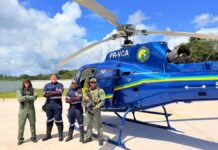 Resgate aeromédico socorre vítima de tiro acidental no interior do Acre Helicóptero de resgate pousado em área rural enquanto equipe de socorro atende pessoa deitada em uma maca no solo.