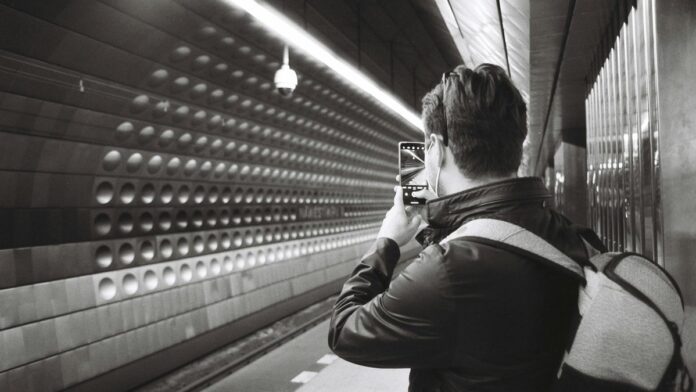 A man photographing the Prague subway station interior with his smartphone.
