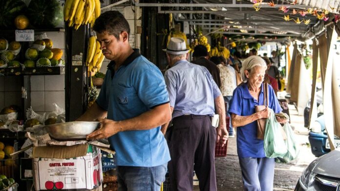 A busy street market with people shopping for fresh produce and fruits displayed on stalls.