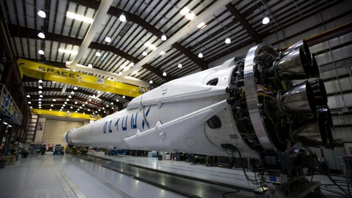 A SpaceX Falcon rocket displayed in a spacious hangar under bright industrial lights.
