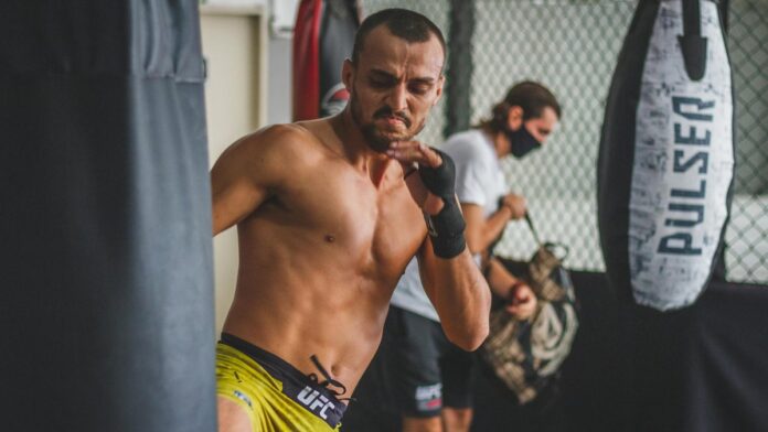 A determined man fiercely trains with a heavy bag inside a gym setting, showcasing athletic focus and strength.