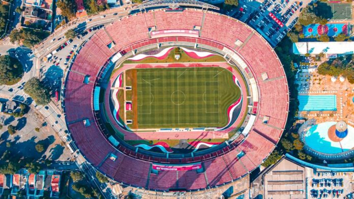 High-angle aerial shot of Morumbi Stadium in São Paulo, featuring the vibrant green field and red seating.