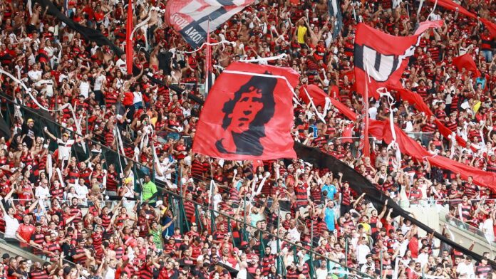 Excited soccer fans in red and black cheer at Maracanã Stadium, Rio de Janeiro.