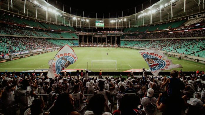 Energetic soccer fans cheer during a night match at a large stadium, creating an exciting atmosphere.