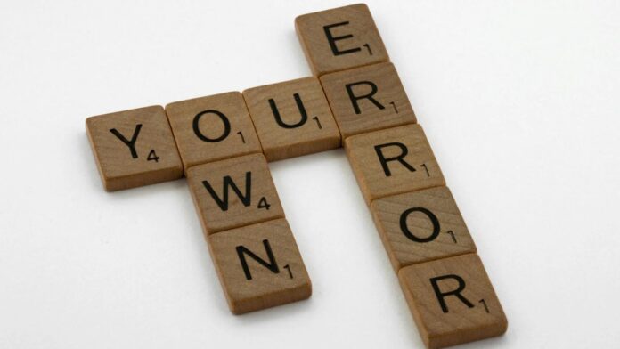 Wooden Scrabble tiles forming the motivational phrase 'Own Your Error' on a white background.