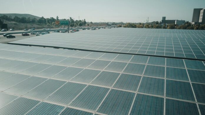 Rows of solar panels near a highway capture renewable energy under a clear sky.