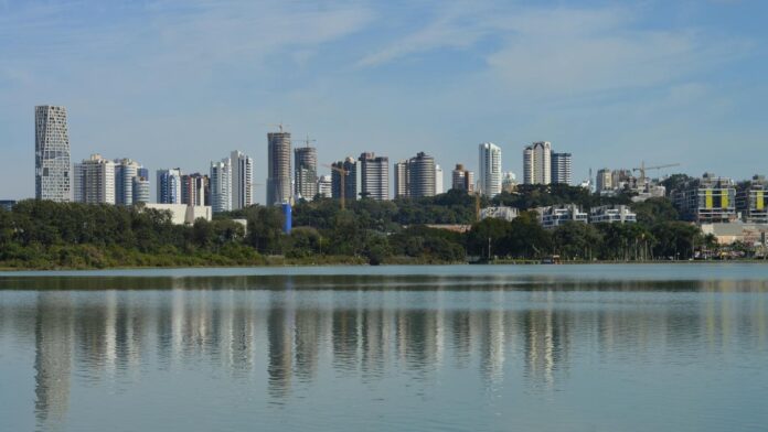 Skyline of Curitiba, Brazil, reflecting on a serene lake under a clear blue sky.
