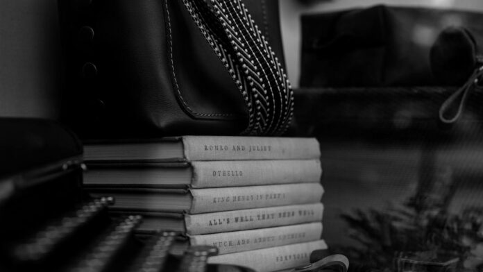 Monochrome photo of classic books stacked with a typewriter and leather bag.