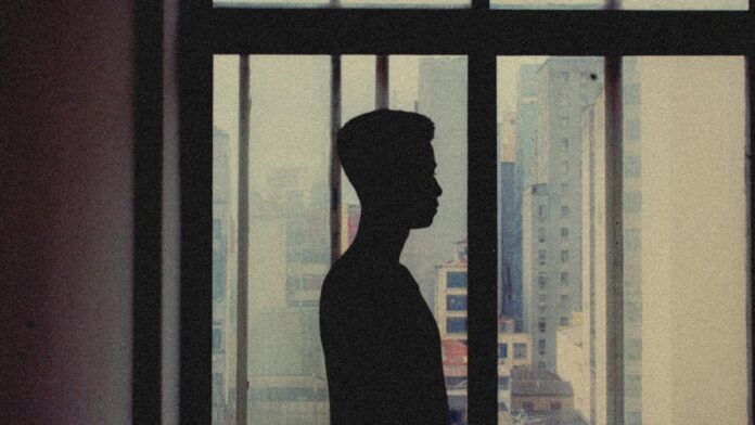 Silhouette of a person looking out a city apartment window showcasing an abstract urban landscape.