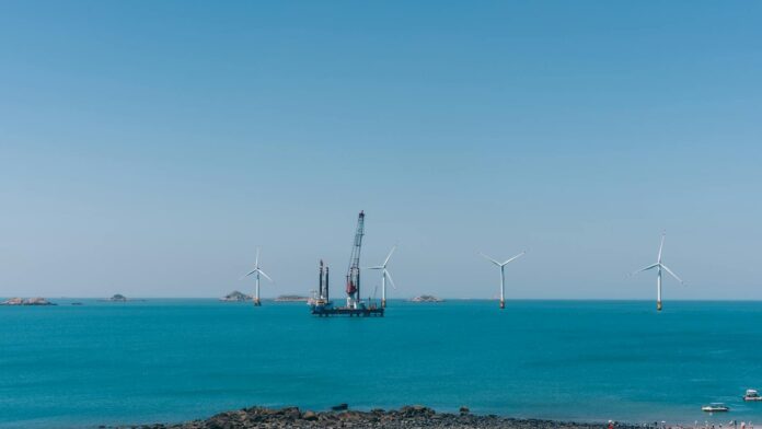 A serene view of offshore wind turbines against a clear blue sky with calm ocean waters.