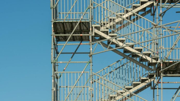 Close-up of metal scaffolding structure with stairs against a clear blue sky, illustrating construction and industrial themes