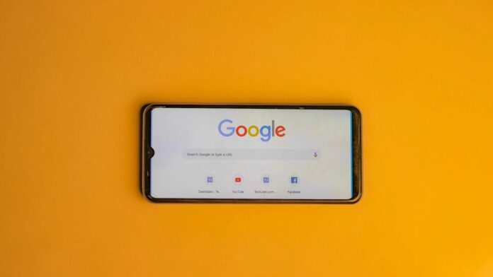 Smartphone displaying Google search page on a vibrant yellow background.