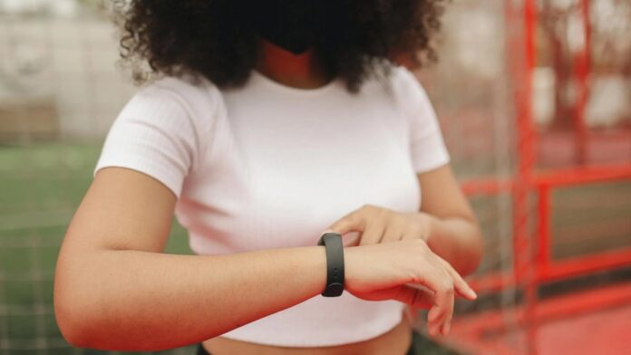 s4-5090a9844cf4-2 Young woman wearing a fitness tracker, checking time in an outdoor sports area.