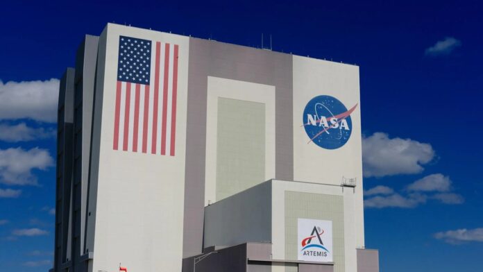 The iconic NASA Vehicle Assembly Building at Kennedy Space Center in bright daylight.