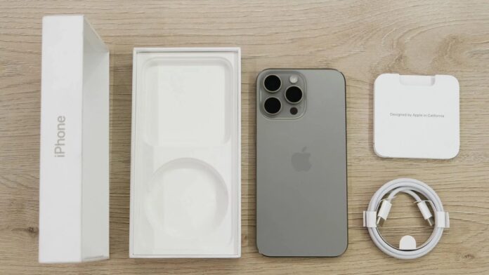 Flat lay view of the newest Apple iPhone model, box, and charging accessories on a wooden table.