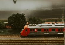 Governo de São Paulo cria centro integrado para vítimas com deficiência no Metrô Aerial view of a red train passing through urban tracks beside a river in São Paulo.