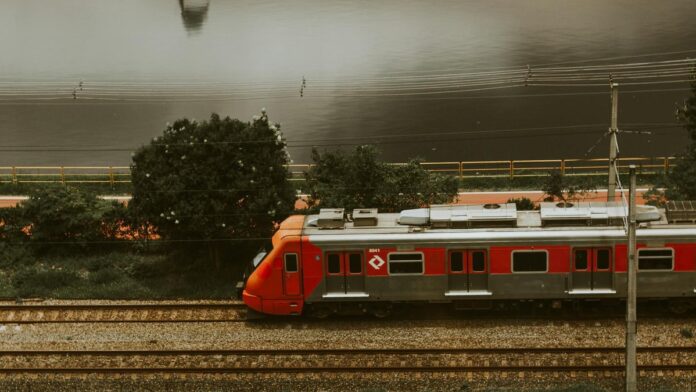 Aerial view of a red train passing through urban tracks beside a river in São Paulo.