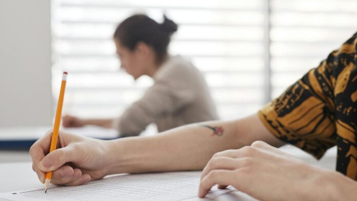 Close-up of student's hands writing on exam sheet, indoors with blurred background.