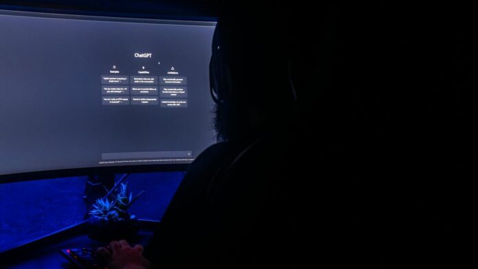 Silhouette of a person using ChatGPT on a computer screen in a dark room, highlighting digital interaction.