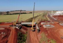 Cidades do Paraná recebem reconhecimento por desempenho em projetos financiados: modelo pode inspirar o País Aerial view of bridge construction site in Cidade Industrial II, Brazil, highlighting cranes and machinery.