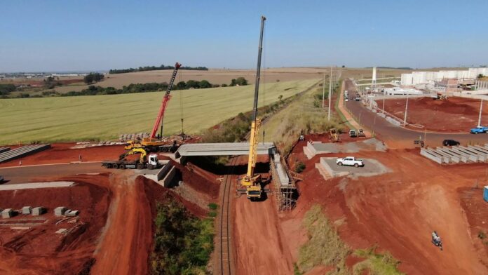 Aerial view of bridge construction site in Cidade Industrial II, Brazil, highlighting cranes and machinery.