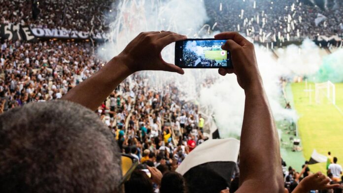 Thrilling football match scene with fans capturing the moment on a smartphone from the stadium stands.