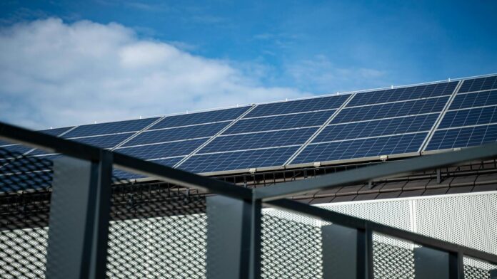 s4-75edee89db64-3 Close-up view of modern solar panels on a rooftop against a clear blue sky, representing clean energy.