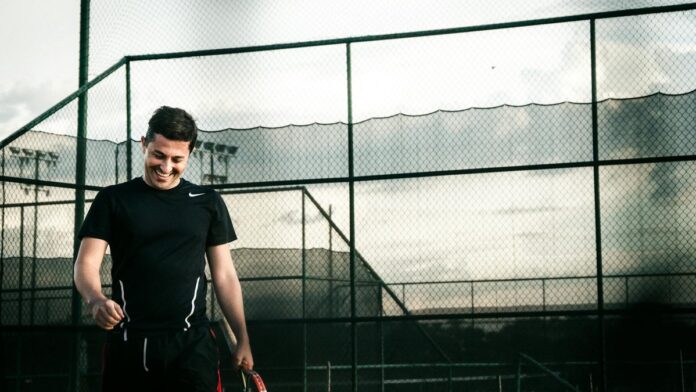 s4-7a5718a50c55 A happy tennis player smiles while holding a racket on an outdoor court.